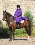 EQUIDRY women's long waterproof horse riding coat in deep purple side view rider sat on horse showing storm skirts 