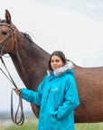 EQUIDRY Evolution Lux Women's Warm Waterproof Winter Horse Riding Coat Thick Fleece Lining with Faux Fur Trim Hood in turquoise rider stood with horse