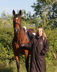 EQUIDRY women's long waterproof horse riding coat in rich brown/cream modelled by rider stood with horse