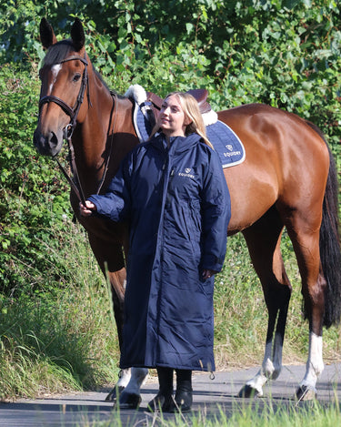 EQUIDRY women's long waterproof horse riding coat in navy/cream worn by rider walking with horse