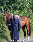 EQUIDRY women's long waterproof horse riding coat in navy/cream worn by rider walking with horse