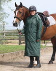 EQUIDRY women's long waterproof horse riding coat in black forest green/green shown by rider stood with horse