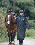 EQUIDRY women's long waterproof horse riding coat in black/turquoise modelled by rider walking with horse 