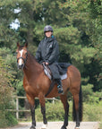 EQUIDRY women's long waterproof horse riding coat in black/turquoise modelled by rider hacking on horse