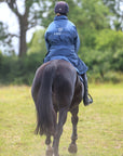 EQUIDRY women's thin fleece stowaway hood long waterproof horse riding coat in steel blue on horse behind 