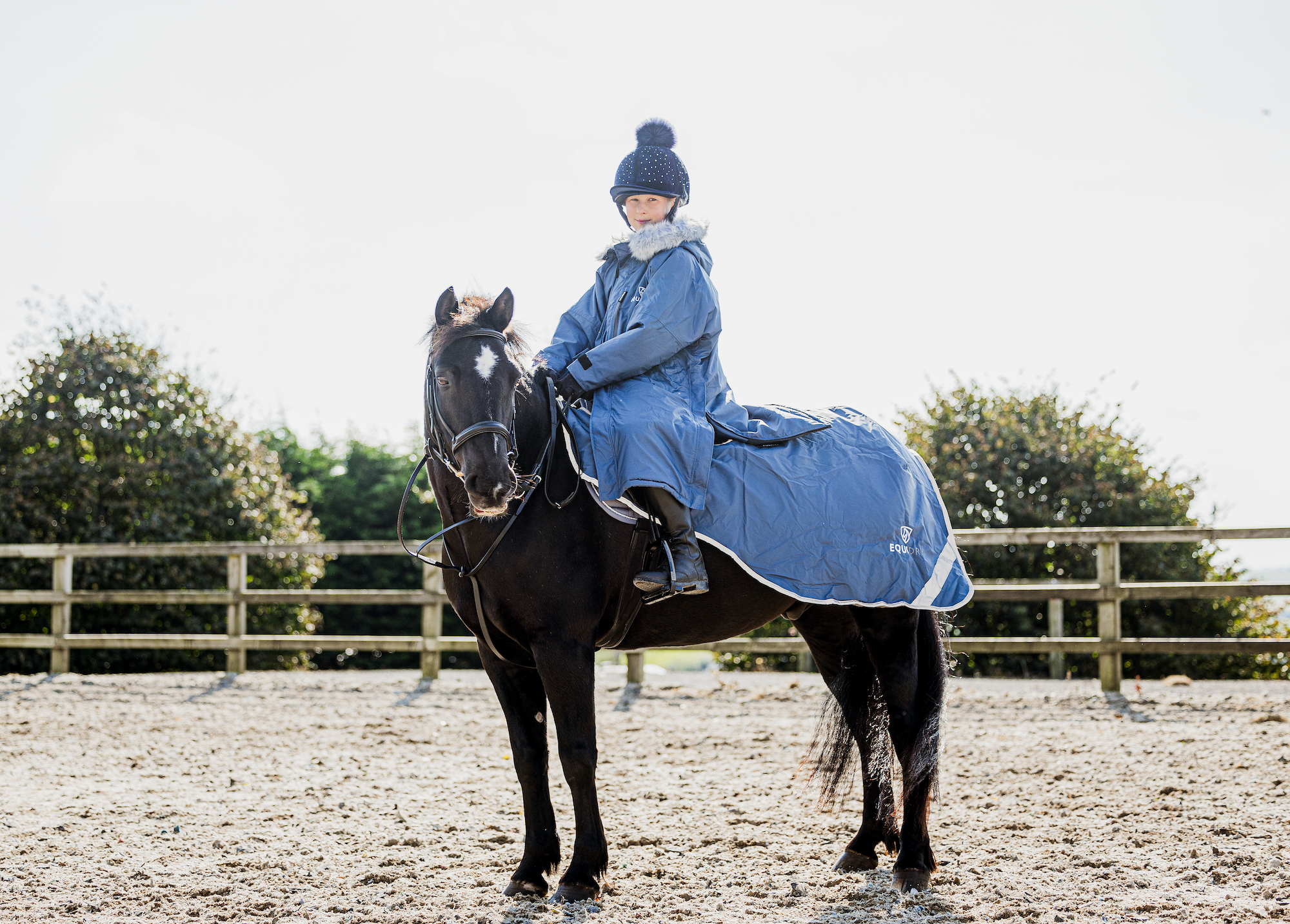 EQUIDRY Evolution Lux children's Warm Waterproof Winter Horse Riding Coat Thick Fleece Lining with Faux Fur Trim Hood being shown in steel blue on horse 