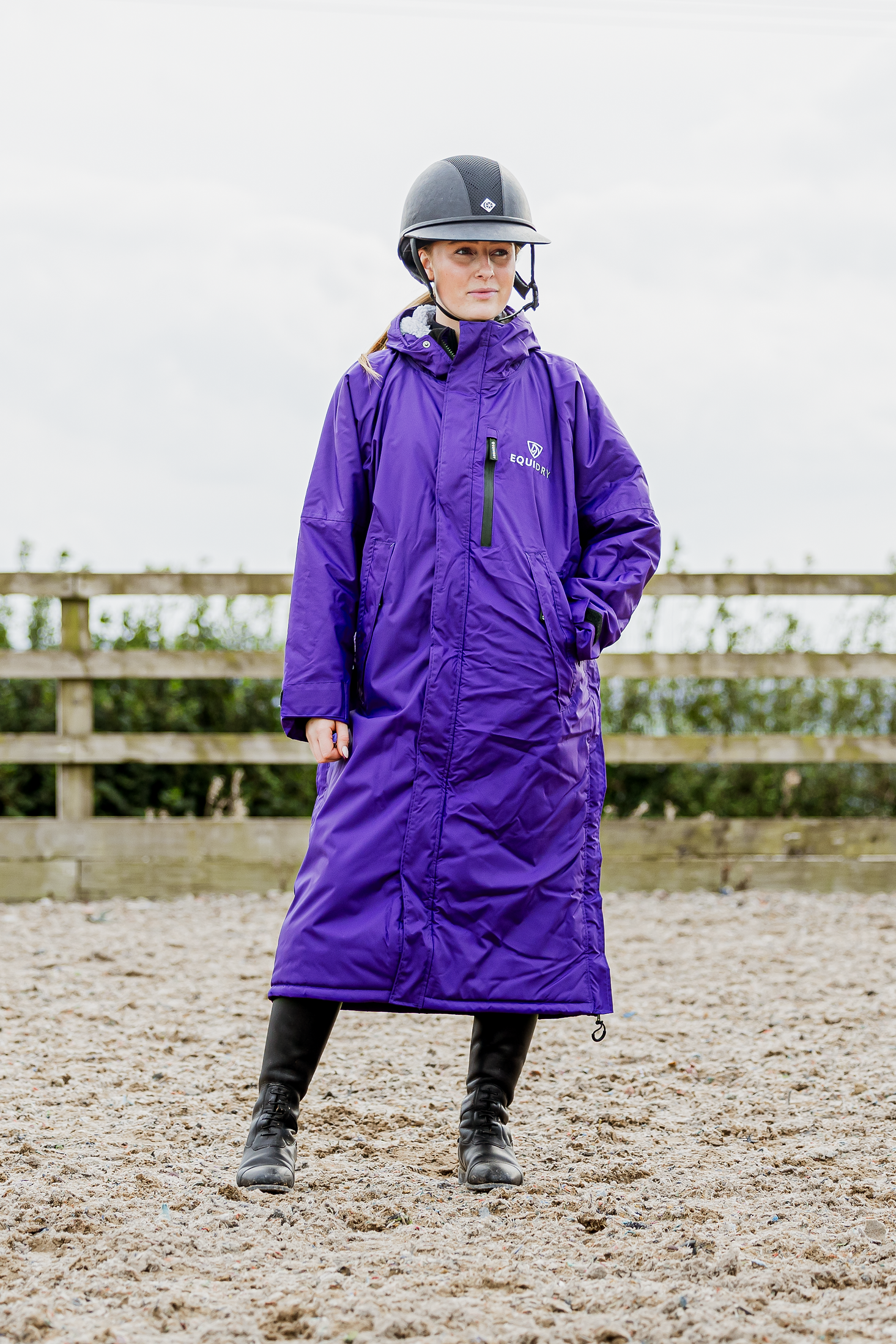 EQUIDRY women's long waterproof horse riding coat in deep purple modelled by rider in arena 