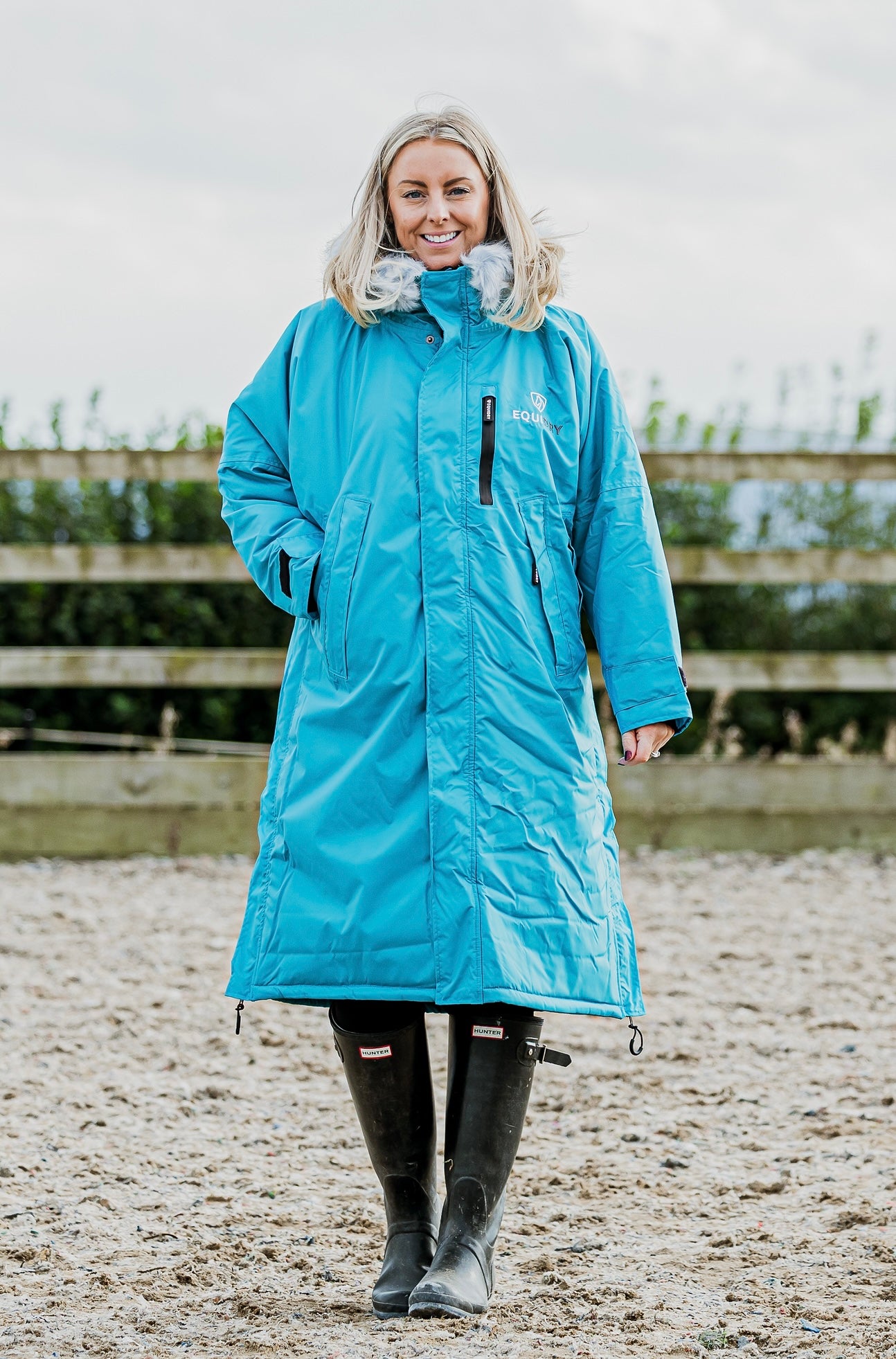 EQUIDRY Evolution Lux Women's Warm Waterproof Winter Horse Riding Coat Thick Fleece Lining with Faux Fur Trim Hood in turquoise rider in arena 