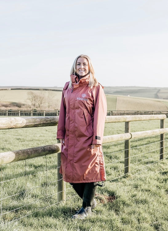 EQUIDRY chestnut equmac lightweight adjustable long riding coat modelled by lady walking in field 