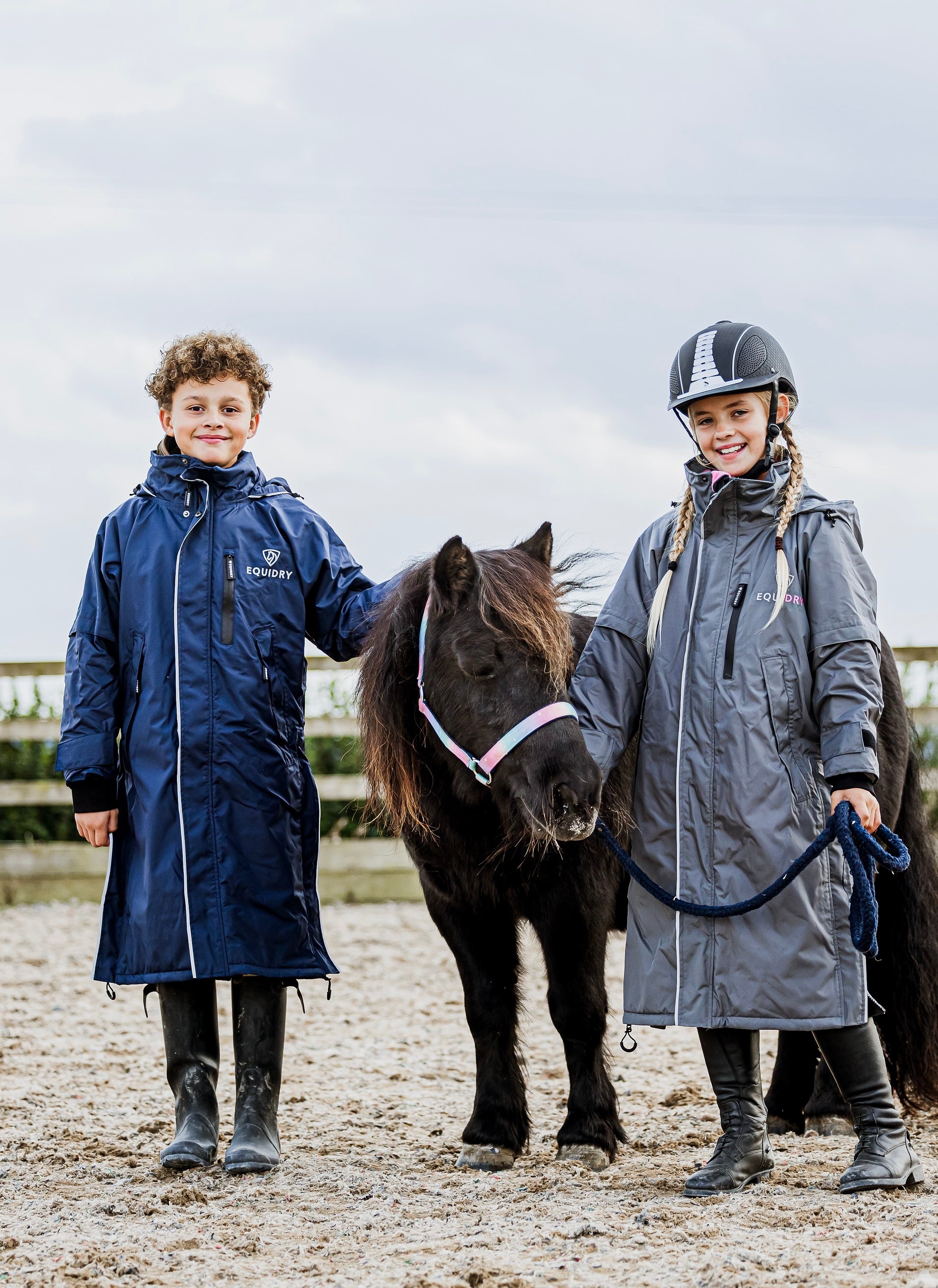 EQUIDRY waterproof horse riding raincoat thin fleece pro ride reflective in navy and charcoal/pale pink children's kids stood with shetland in arena 