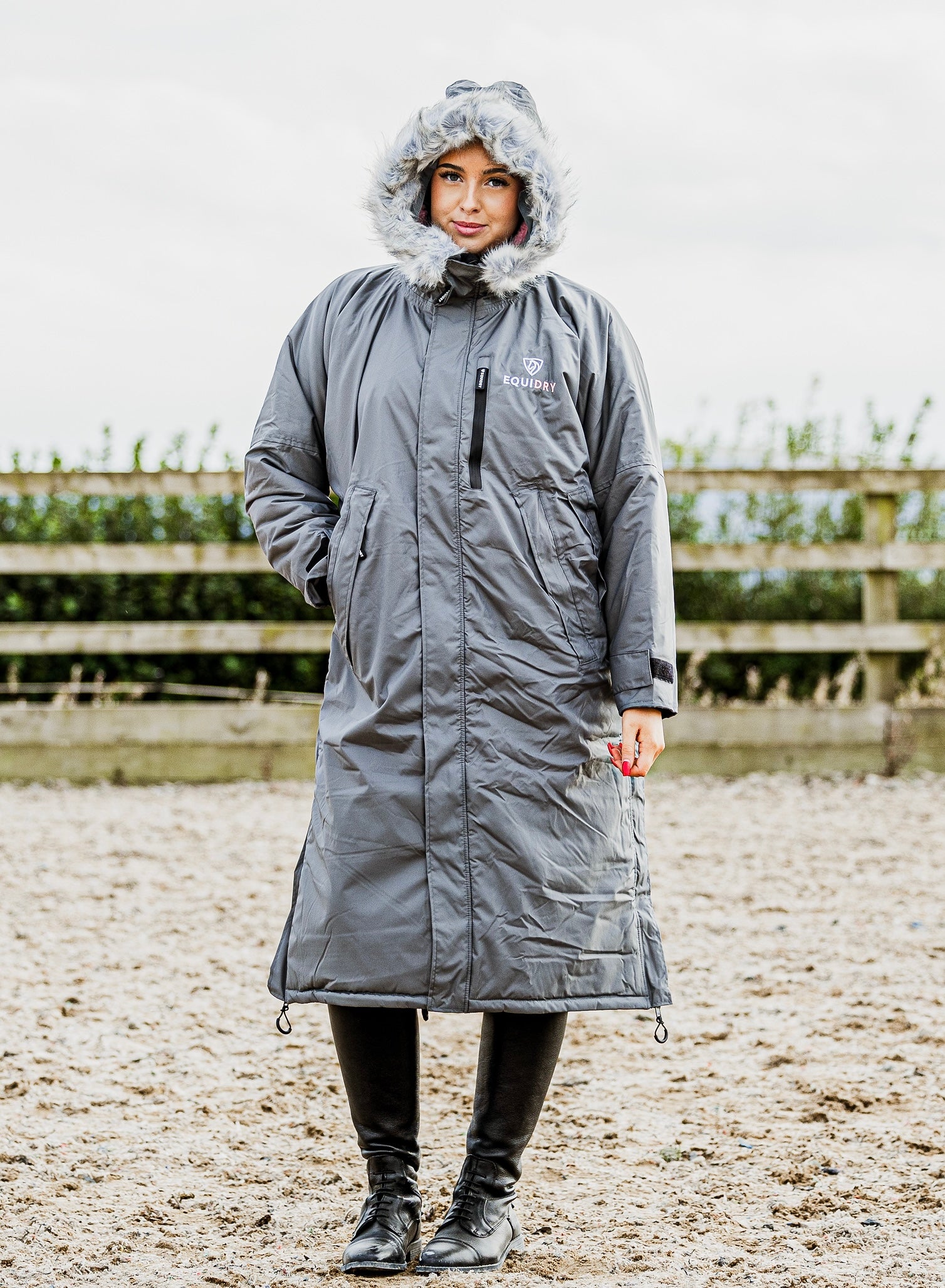 EQUIDRY Evolution Lux Women's Warm Waterproof Winter Horse Riding Coat Thick Fleece Lining with Faux Fur Trim Hood charcoal/pale pink modelled by rider in arena with hood up