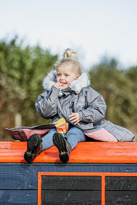 EQUIDRY Evolution Lux children's Warm Waterproof Winter Horse Riding Coat Thick Fleece Lining with Faux Fur Trim Hood being shown in charcoal/pale pink by little girl on cross country jump 