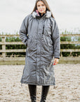 EQUIDRY Evolution Lux Women's Warm Waterproof Winter Horse Riding Coat Thick Fleece Lining with Faux Fur Trim Hood charcoal/pale pink modelled by rider in arena, full front view of coat