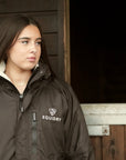 EQUIDRY women's long waterproof horse riding coat in rich brown/cream shown being worn on the yard