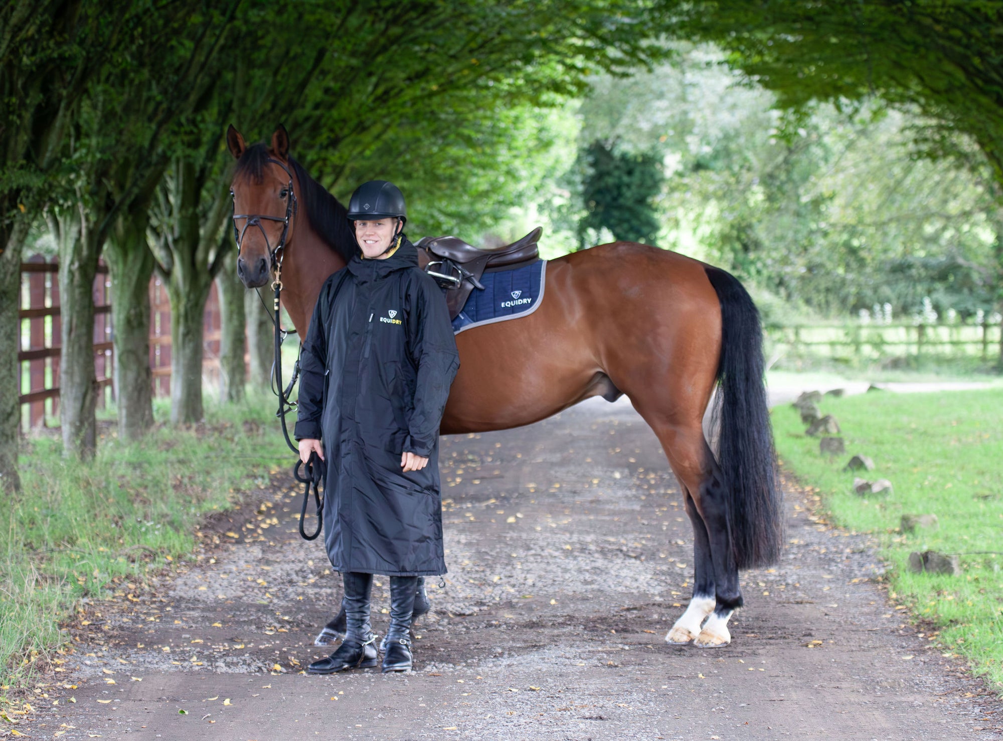  EQUIDRY men&#39;s long waterproof horse riding coat in Black/Yellow being modelled by male rider holding horse