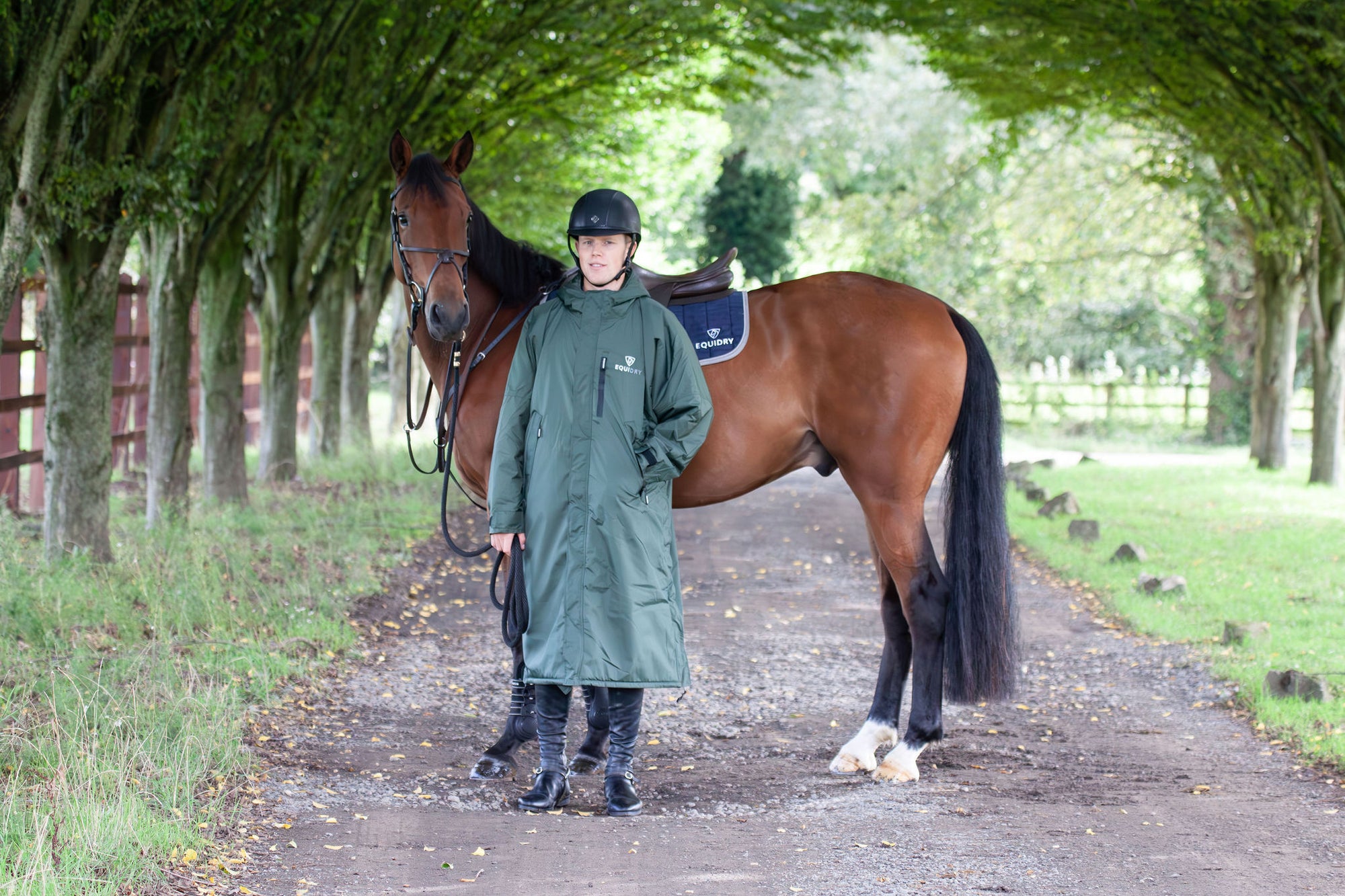 Black Forest Green EQUIDRY Equimac long waterproof raincoat worn by male rider stood with horse