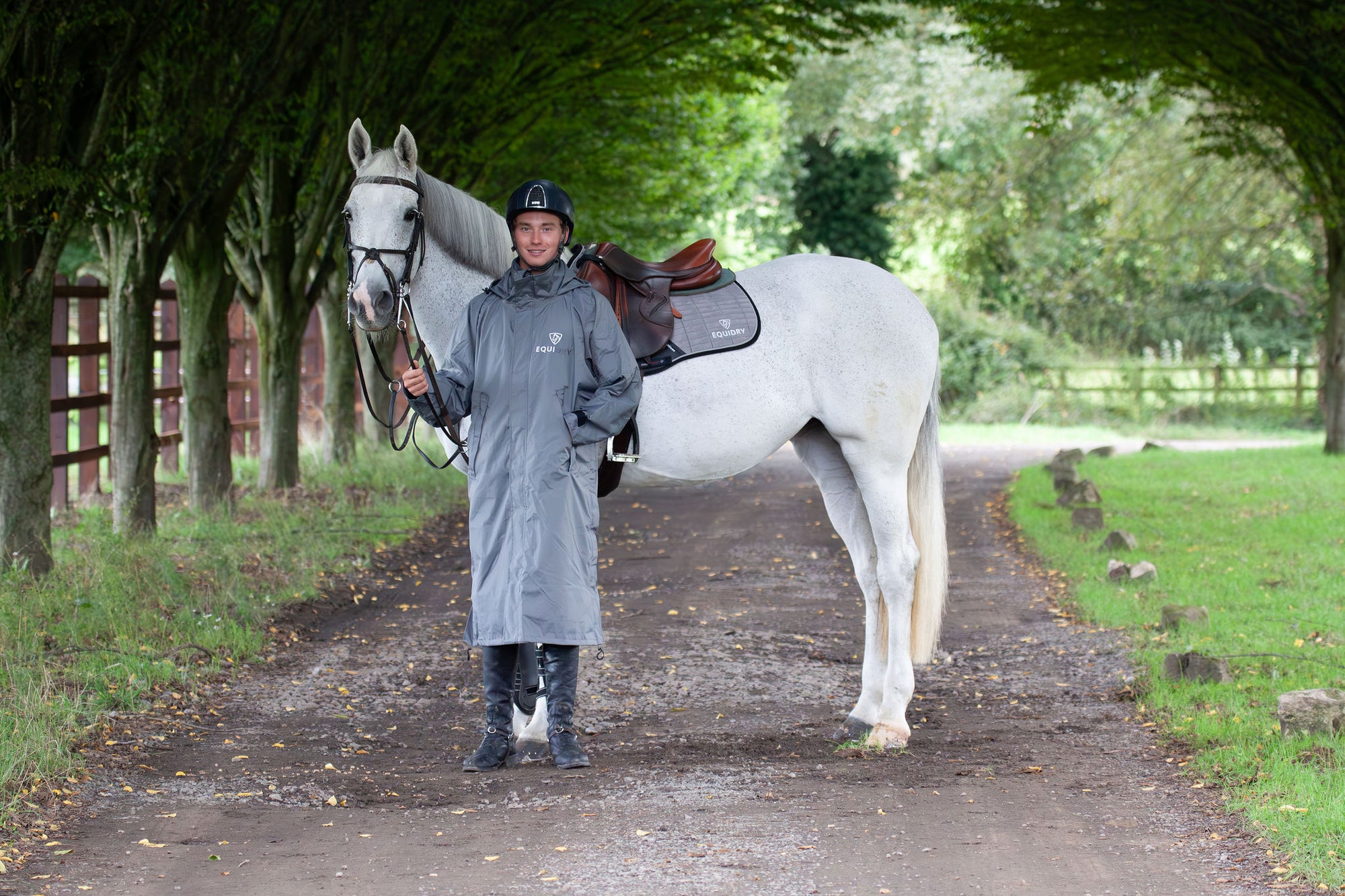 Evolution Equimac Men&#39;s Lightweight Waterproof Horse Riding Raincoat in charcoal modelled by male rider with horse