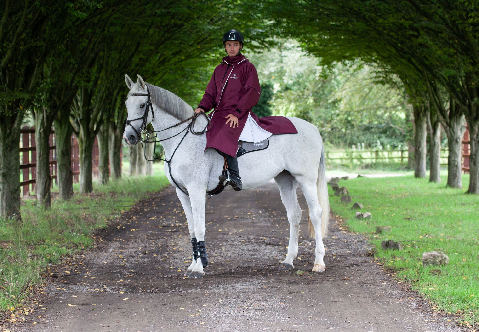 Evolution Reflective Men's Lightweight Waterproof Horse Riding Coat in plum worn by male rider on horse showing storm skirts 