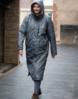 EQUIDRY women's long waterproof horse riding coat in charcoal/pale pink showing groom on yard sheltering from the rain 