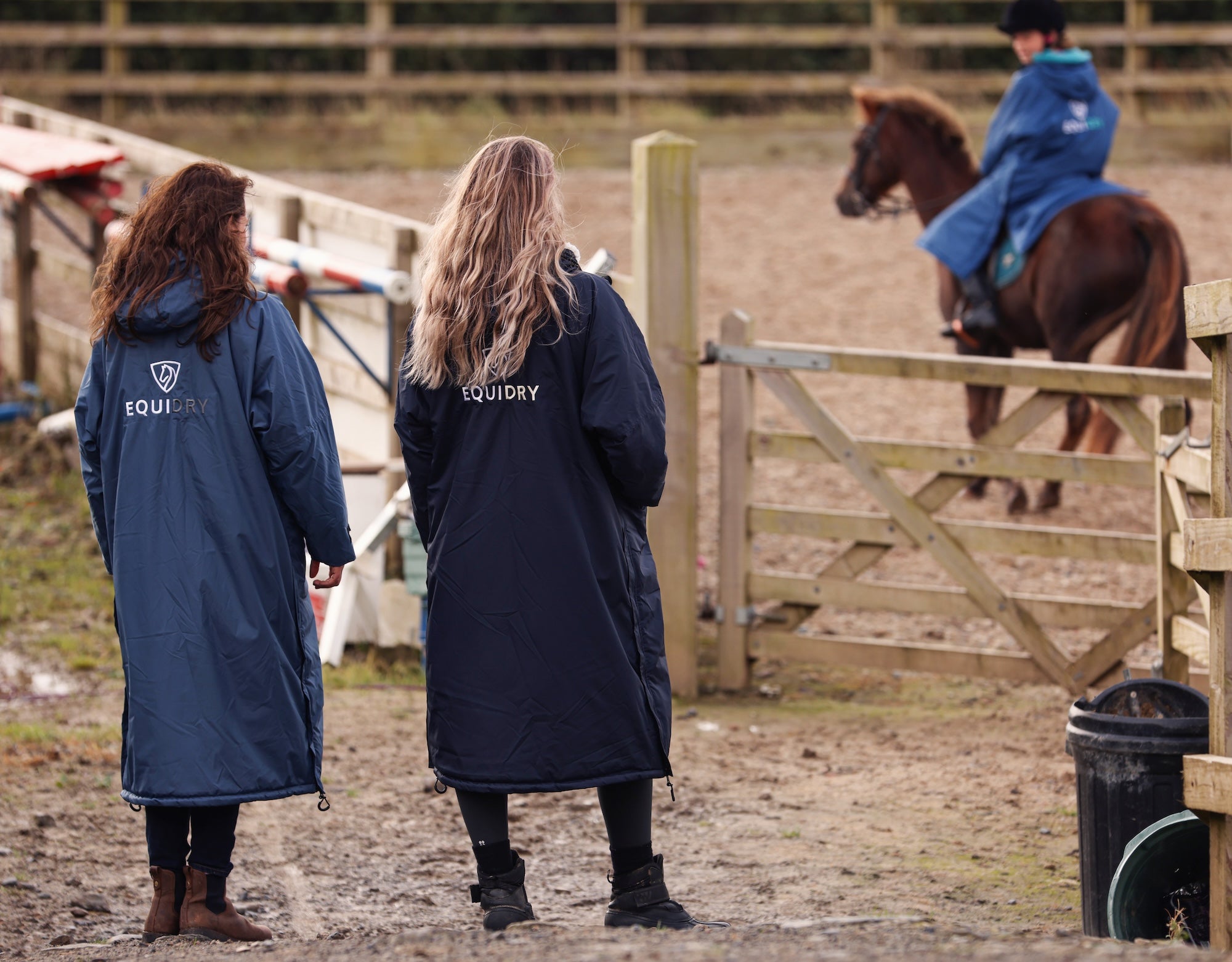 EQUIDRY women's long waterproof horse riding coat in navy/cream mums stood spectating riding lesson by arena, back of coats 