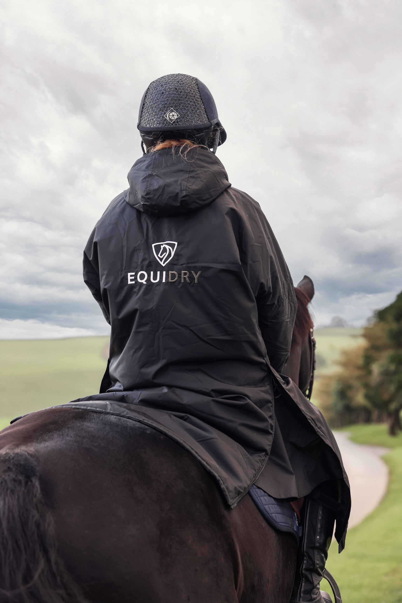 EQUIDRY women's long waterproof horse riding coat in black/olive modelled by rider out hacking horse