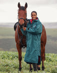 EQUIDRY women's long waterproof horse riding coat in Teal/Peacock Pink modelled by rider stood with horse 